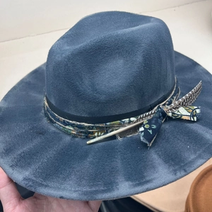 Detail of dark grey fedora hat featuring ethnic ribbon, decorative rope, and real feather