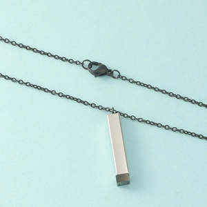 Gros plan d'un pendentif cubique argent et noir sur une chaîne en métal noir mat