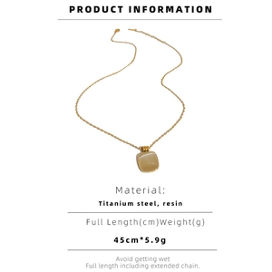 Détail du pendentif carré en résine beige sur une chaîne dorée en acier titane