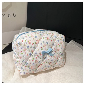 Detail of floral quilted makeup bag with blue zipper and bow on a soft fabric base