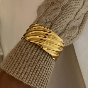 Polished 18k gold stainless steel wavy bangle worn over a beige knitted sweater