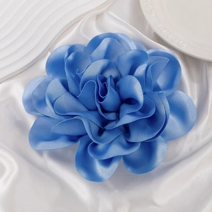 Detailed close-up of large blue silk rose brooch on elegant white textured backdrop