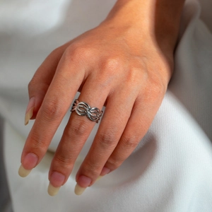 Close-up of twisted woven hollow silver ring on finger with soft fabric background