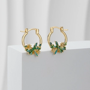 Detailed close-up of golden dragonfly and daisy enamel lever back earrings on white stone