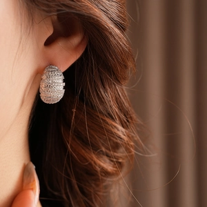 Macro shot of a silver oval earring set with sparkling zircons worn on ear