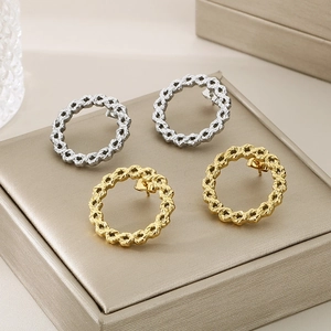 Macro detail of gold and silver braided twist stud earrings on a textured jewelry box