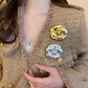Detail of gold and silver metal camellia flower brooches on a tweed jacket