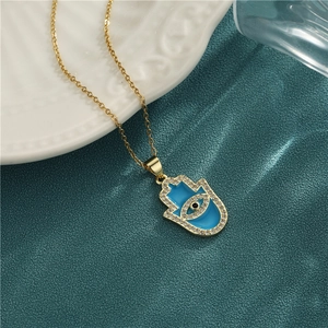 18K gold Hamsa Hand necklace with blue enamel and sparkling zircon on green fabric