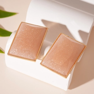 Pink resin rectangle stud earrings with gold trim and glitter on white display stand