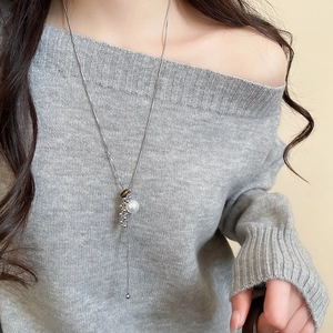 Long tiger eye pearl necklace with silver metal tassels on a grey knit sweater