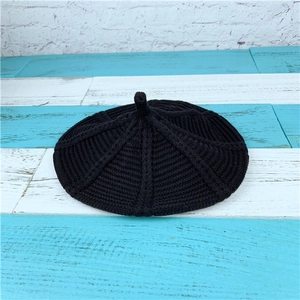 Close-up of black cable knit beret showing textured radial ribbing and top stem detail