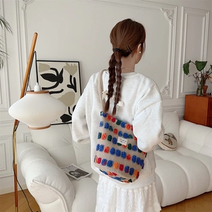 Detailed back view of a plush beige bucket bag decorated with colorful 3D pom-poms