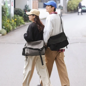 Men's large canvas messenger bag in grey and black shown in a casual street style look