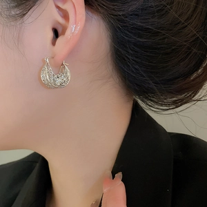 Detailed close-up of a silver hollowed-out flower hoop earring worn by a model