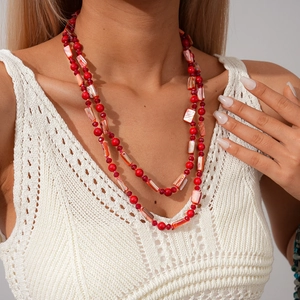 Détail du collier bohème en perles rouges et fragments de coquillages sur tricot blanc