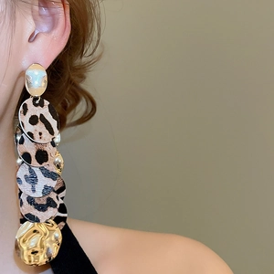 Détail de boucles d'oreilles pendantes en cuir léopard et disques dorés sur un mannequin