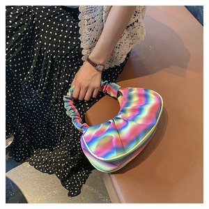Detail of a rainbow gradient ruched dumpling bag held by a model in a stylish outfit