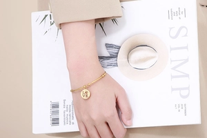 Detailed shot of a gold open bangle with a LOVE engraved pendant worn by a model