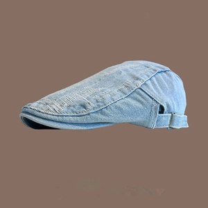Detail of light blue washed denim beret featuring distressed edges and adjustable metal buckle