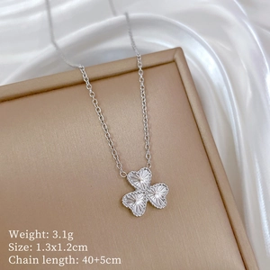 Macro detail of a silver clover pendant with heart-shaped leaves on soft white silk