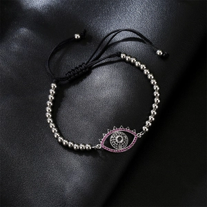 Detail of evil eye charm with pink cubic zirconia on black braided bead bracelet