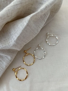 Macro shot of twisted metal hoop earrings in gold and silver finish on linen fabric
