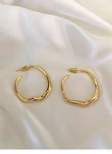 Close-up of golden irregular round hoop earrings on soft white silk background