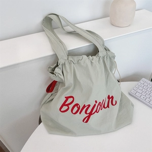Close-up of sage green canvas bag with red Bonjour text and drawstring closure detail