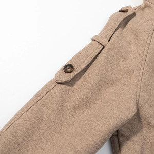 Detail of wool coat shoulder strap with brown button on khaki textured fabric