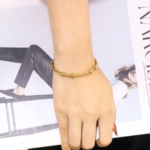 Adjustable golden stainless steel wire bracelet with beads worn by model against magazine