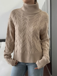 Detail of loose beige knit sweater showing the intricate wavy weave pattern and high collar