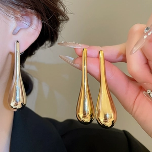Close-up of a large gold teardrop pendant earring worn to show its sleek metallic texture