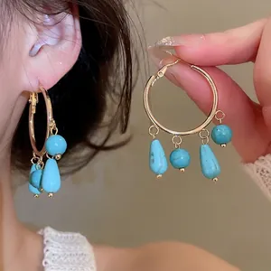 Ethnic style gold hoop earrings with turquoise stone tassels shown in a hand-held detail view