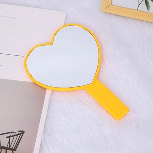 Close-up of yellow heart-shaped handheld mirror with handle on white faux fur background