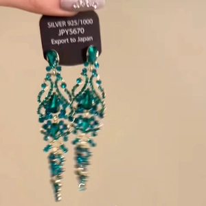 Detail of long tassel earrings with green crystal and 925 silver certification tag