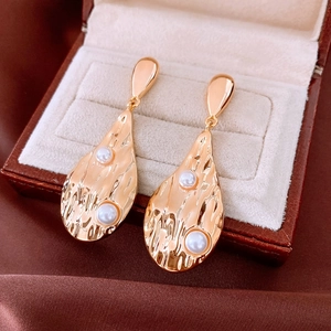 Détail macro de boucles d'oreilles goutte plaquées or 18K avec texture martelée et perles