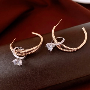 Detail of twisted rose gold hoop earring with silver pendant and sparkling zircon