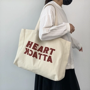 Off-white canvas tote bag with red Heart Attack print shown on a female model