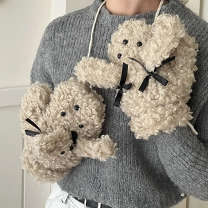Détail de moufles pelucheuses beige en forme de chien avec de jolis nœuds en satin noir