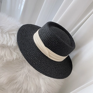 Detailed texture of black straw flat top hat with beige ribbon on soft white fur