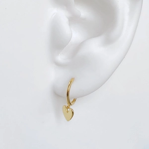 Close-up of elegant gold heart hoop earrings worn on model with a white background