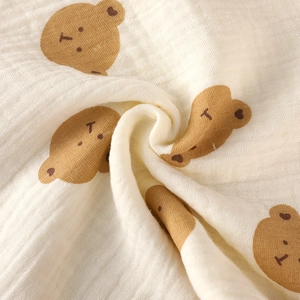 Close-up of soft beige muslin fabric with brown cartoon bear prints and crinkled texture