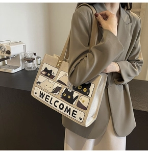 Detail of beige canvas tote bag with cartoon cat print and brown shoulder straps