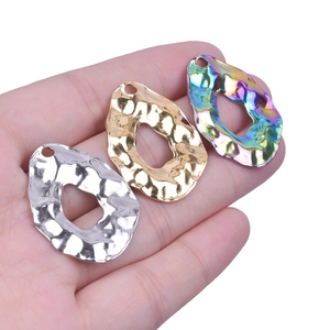 Hand holding three geometric hammered metal pendants in gold, silver, and rainbow colors