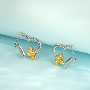 Detail of silver heart hoop earrings featuring a gold 3D bee over soft water ripples