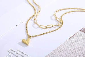 Détail d'un collier doré multicouche avec chaîne trombone et pendentif cœur en relief