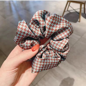 Detailansicht eines handgehaltenen Satin-Haargummis mit rot-blauem Hahnentrittmuster