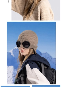 Detail of brown knit pom-pom hat with integrated aviator goggles on snowy mountain backdrop