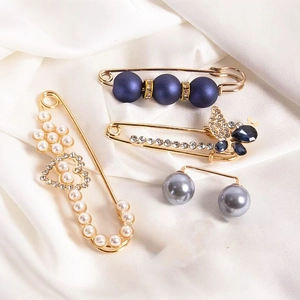 Detail of luxury pearl and rhinestone brooch pins set on elegant white silk background