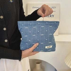 Detail of blue denim cosmetic bag with white bows and heart patterns being held by a hand